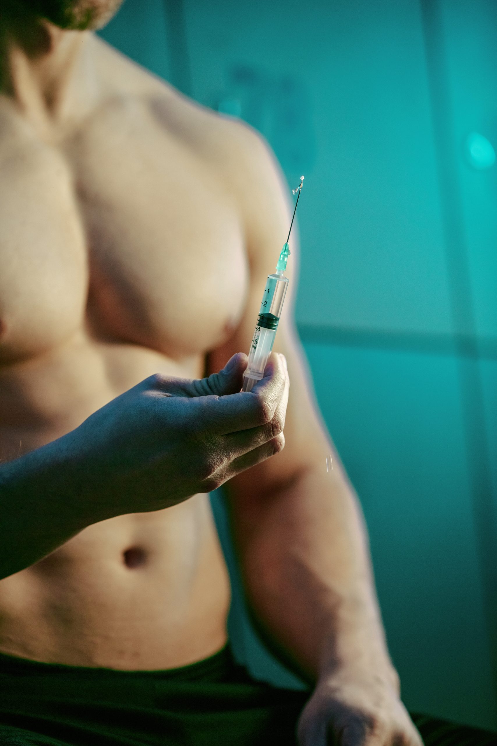 Close up of muscular build man with injection of anabolic steroids in gym's changing room.